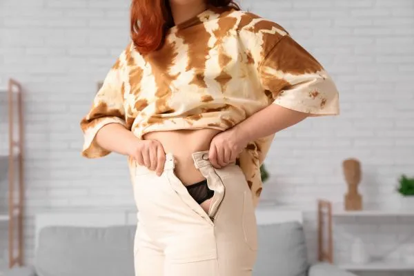 Image of woman trying to do her trousers up after pregnancy weight gain Bedworth